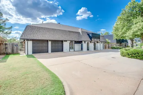 Front exterior with white painted brick, gray mansard-style shingle roof, three-car garage, and wide concrete driveway at Brompton Manor, Oklahoma City