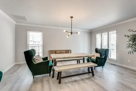Dining room with wood farmhouse table, bench seating, two emerald green velvet wingback chairs, and a brass globe chandelier at Brompton Manor, Oklahoma City