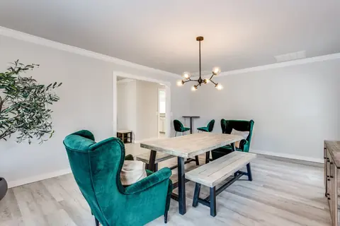 Dining area with green velvet armchairs, wood table with black-frame benches, sputnik chandelier, and an olive tree accent at Brompton Manor, Oklahoma City