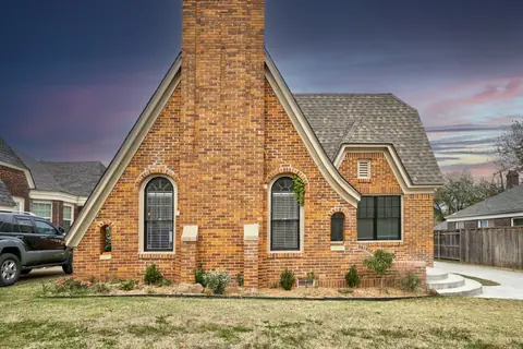 Red-brick Tudor-style exterior with arched windows, steep gables, and tall brick chimney at dusk at Capital Manor, Oklahoma City