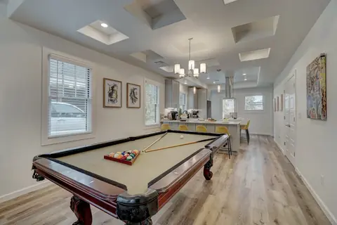 Pool table with racked balls in the open-concept game room flowing into the kitchen with yellow bar-stool seating at Capital Manor, Oklahoma City