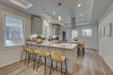 Quartz breakfast bar lined with yellow velvet stools under pendant lighting in the bright kitchen at Capital Manor, Oklahoma City