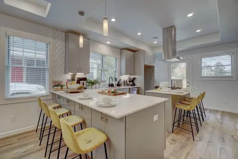 Open kitchen with two white quartz islands, yellow velvet bar stools, pendant lights, and stainless vent hood at Capital Manor, Oklahoma City