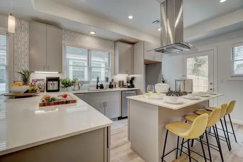 Kitchen island with gas cooktop and stainless hood beside a quartz counter staged with fresh fruit and cutting board at Capital Manor, Oklahoma City