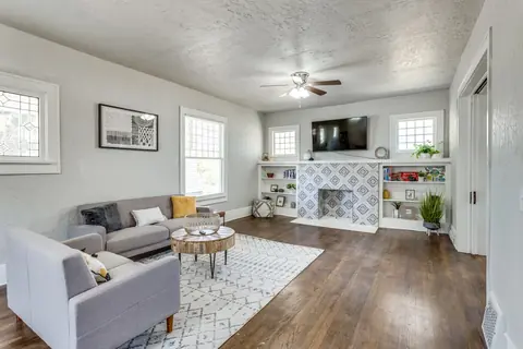 Living room with gray sofas, round wood coffee table, patterned tile fireplace and wall-mounted TV at Classen Manor, Oklahoma City