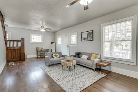 Open living room with two gray sofas on a patterned rug and the original dark-wood staircase at Classen Manor, Oklahoma City