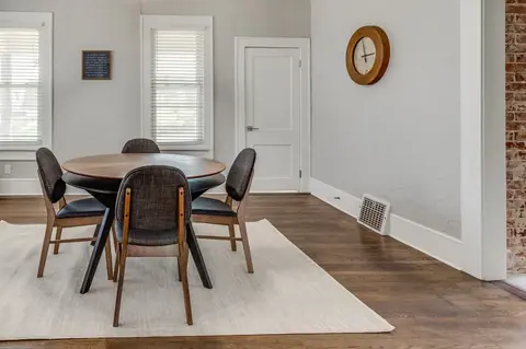 Dining room with round wood table, four upholstered chairs, wall clock and exposed brick accent at Classen Manor, Oklahoma City