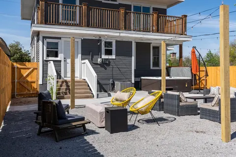 Classen Manor's backyard: hot tub, patio lounges, fire-pit seating and cafe lights below the balcony