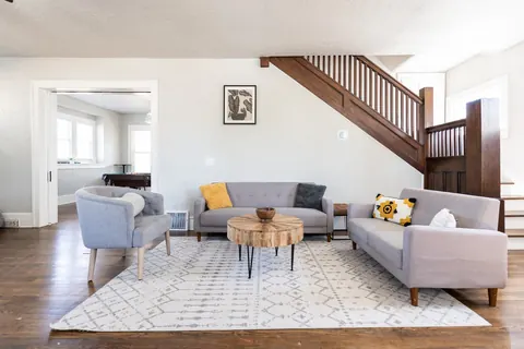 Classen Manor living room under the original wood staircase, twin gray sofas around a live-edge table