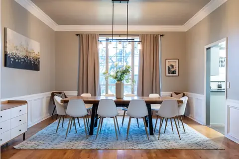 Formal dining room with long wood table, white chairs, and linear chandelier in front of a tall window at Gaillardia Manor, Oklahoma City