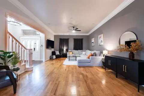 Living room with light gray sectional, ceiling fan, black sideboard, and staircase entry with hardwood floors at Gaillardia Manor, Oklahoma City