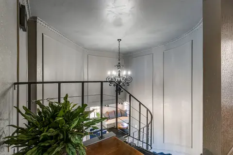 Curved wrought-iron staircase with chandelier and paneled walls overlooking the living room seating below at Lakefront Manor, Oklahoma City