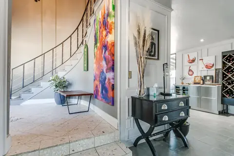 Curved staircase entry with gallery art, console table, and wine storage at Lakefront Manor, Oklahoma City
