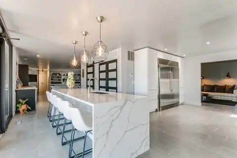 Marble waterfall island with pendant lights, bar seating, and built-in refrigerator columns in the open kitchen at Lakefront Manor, Oklahoma City