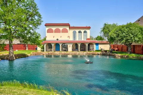 Turquoise backyard pond with spray fountain in front of the red-roofed Spanish-style home on a sunny day at Lakeside Manor, Oklahoma City