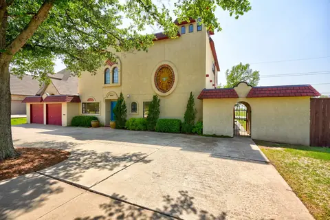 Street-facing stucco facade with sunburst mosaic round window and arched courtyard gate beside the driveway at Lakeside Manor, Oklahoma City
