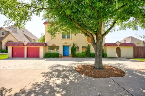 Front exterior with two red garage doors, bright blue front door and a large shade tree over the wide concrete driveway at Lakeside Manor, Oklahoma City