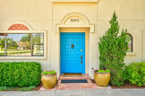 Bright blue paneled front door with lion knocker, terracotta tile step, gold planters and green shrubs at Lakeside Manor, Oklahoma City