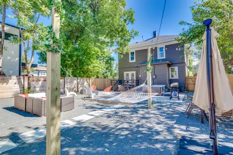 Fenced backyard with rope hammock, hot tub, string lights, wicker lounge seating, and patio umbrella behind the gray two-story Plaza Manor home, Oklahoma City