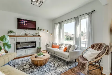 Living room seating area with plush sofa, orange lumbar pillows, rattan accent chair draped in a faux-fur throw, and electric fireplace below the TV at Plaza Manor, Oklahoma City