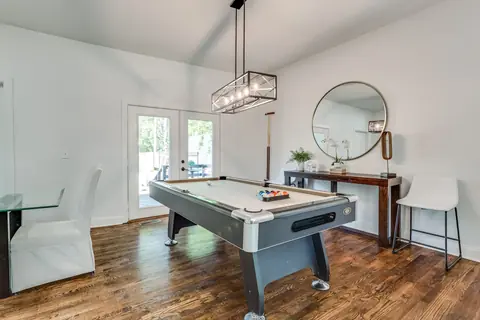 Game room pool table with racked balls beneath a modern chandelier, round mirror over a wood console, and French doors to the backyard at Plaza Manor, Oklahoma City
