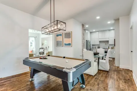 Pool table under a caged linear chandelier in the open game room, looking through to the dining area and kitchen at Plaza Manor, Oklahoma City