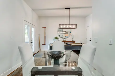 Glass-top dining table with white upholstered chairs, with the pool table and round wall mirror beyond at Plaza Manor, Oklahoma City