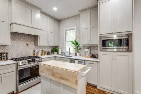 Kitchen with greige shaker cabinets, herringbone tile backsplash, gas range, built-in stainless microwave, and butcher-block island at Plaza Manor, Oklahoma City