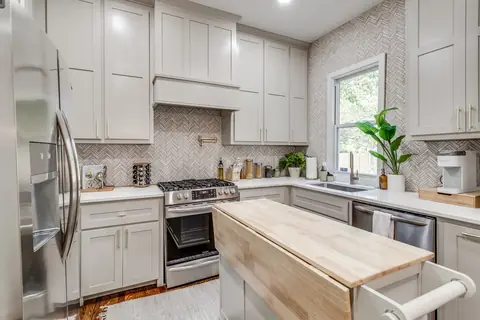 Kitchen with stainless French-door refrigerator, gas stove, undermount sink beneath a sunny window, and rolling butcher-block island at Plaza Manor, Oklahoma City