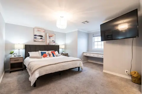 Carpeted bedroom with king bed, dark upholstered headboard, wall-mounted TV and built-in desk nook at Quail Creek Manor, Oklahoma City