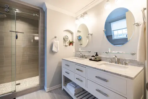 Bathroom with marble-top double vanity, round mirrors and glass walk-in shower at Quail Creek Manor, Oklahoma City