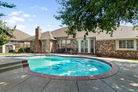 Backyard pool with brick coping and wide concrete patio behind the brick house, with covered patio seating and a storage shed at Remington Manor, Oklahoma City