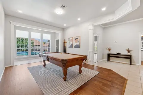 Game room with a wooden pool table, cue rack, and large windows overlooking the backyard pool and patio at Remington Manor, Oklahoma City