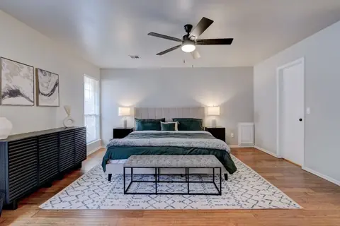 Bedroom with an upholstered bed in green bedding, matching table lamps, upholstered bench, and black slatted dresser at Remington Manor, Oklahoma City