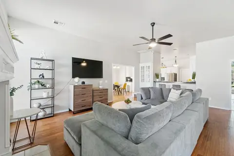 Open-concept living room with large gray sectional sofa, wall-mounted TV, and ceiling fan flowing into the kitchen and dining area at Remington Manor, Oklahoma City