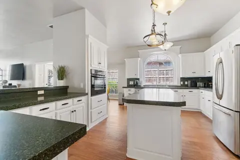 Kitchen with white cabinetry, dark speckled countertops, center island, stainless steel refrigerator, wall oven, and arched window at Remington Manor, Oklahoma City