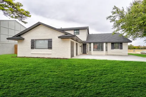 White-painted brick home with black shutters, attached garage, and a wide green front lawn at The Village Manor, Oklahoma City