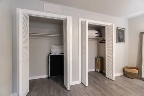 Bedroom closets with white bi-fold doors, shelving, spare pillows, and a folding rollaway guest bed at The Village Manor, Oklahoma City