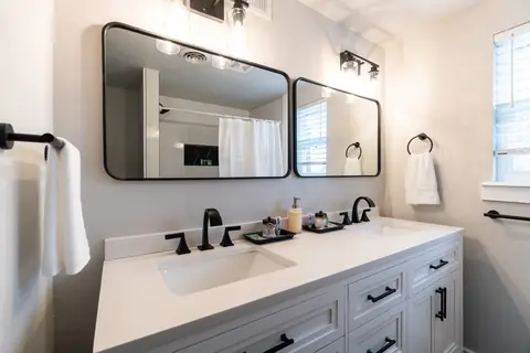 Bathroom with a white double-sink vanity, two black-framed mirrors, matte-black faucets, and white towels at The Village Manor, Oklahoma City