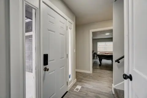 Entry hallway with white front door, keypad lock, and stair rail, looking into the game room with pool table at The Village Manor, Oklahoma City