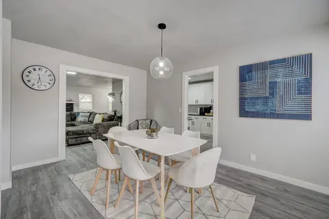 Dining room with a white table for six, globe pendant light, and blue abstract wall art, opening to the living room and kitchen at The Village Manor, Oklahoma City