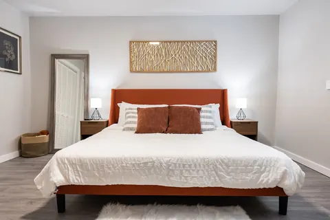 King bedroom at The Village Manor with rust-orange upholstered bed and branch-art wall piece