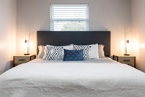 King bedroom at The Village Manor with gray headboard, twin reading lamps and light-wood nightstands