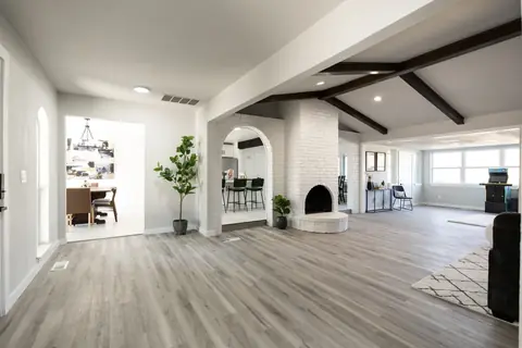 Open-concept main living area with white brick fireplace, arched kitchen passage, dining room, and sunlit game room with arcade cabinet at Will Rogers Manor, Oklahoma City