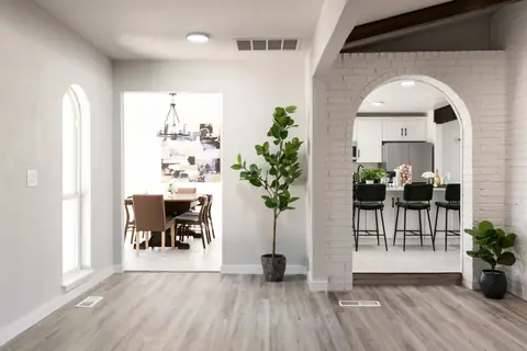 Bright foyer with faux tree, opening to the formal dining room and an arched white-brick passage into the kitchen at Will Rogers Manor, Oklahoma City