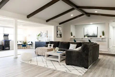 Charcoal sectional with faux-fur throw and whitewashed coffee table, with an arcade machine and navy console in the background at Will Rogers Manor, Oklahoma City