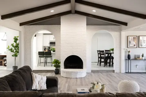 White-painted brick fireplace with arched firebox flanked by twin brick archways into the kitchen and dining room at Will Rogers Manor, Oklahoma City